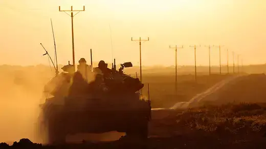 A backlit Israeli army tank moving along the Israeli-Gaza Strip border at sunset