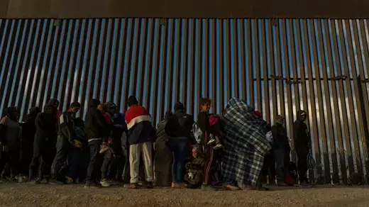 Migrants line up against the border wall in El Paso to surrender to immigration officials on March 25, 2024.
