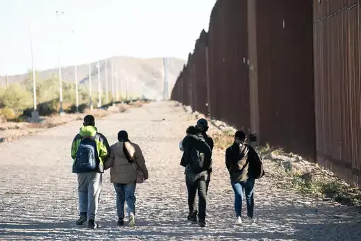 Five people as viewed walking to the left of the U.S. southern border.