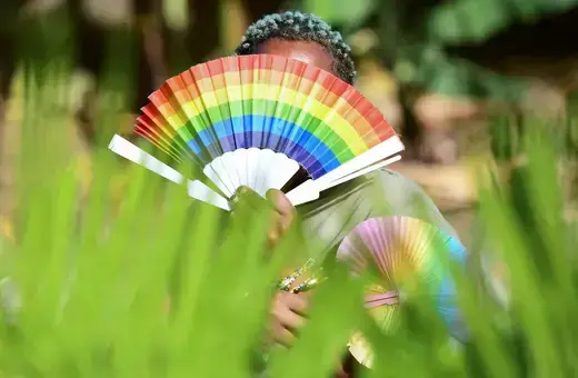 Somone holds up a pride fan with rainbow colors. 