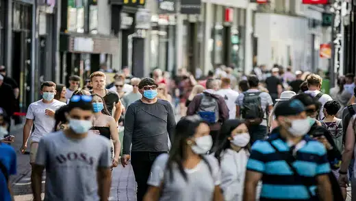 A group of pedestrians walking on a busy sidewalk wearing facemasks.