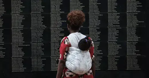 Woman carrying her child reads the names of Rwandan genocide victims.