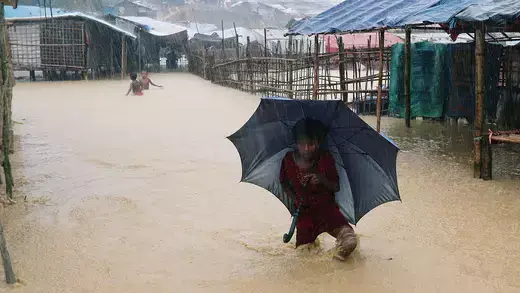 Rohingya refugee girl walks along the water with umbrella across a flooded refugee camp during heavy rain