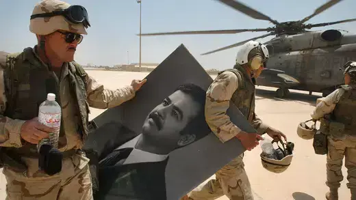 U.S. Marines walk toward a helicopter while carrying a portrait of toppled Iraqi President Saddam Hussein