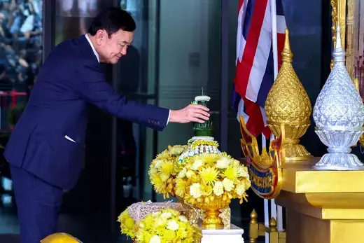 Former Thai prime minister stands at a gold altar with flowers and candles.