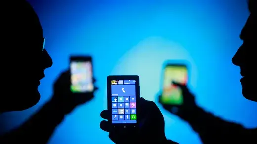 Men are silhouetted against a blue screen as they hold up their smartphones.