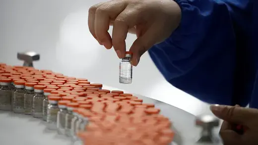 A worker performs a quality check in the packaging phase of a medicine vial.