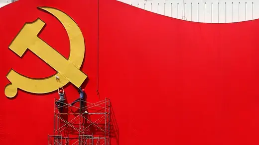 Two workers standing on metal railings to installs a giant red Communist Party flag in Shanghai, China.