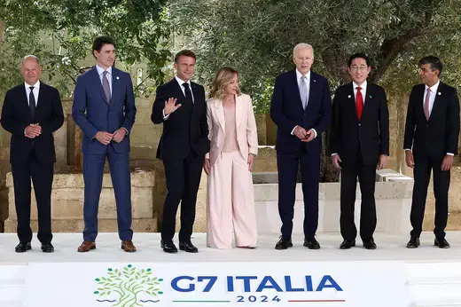 The seven leaders of the G7 countries stand on a stage emblazoned with G7 insignia.