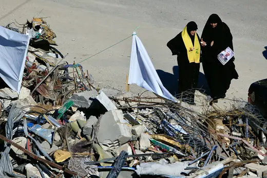 Two veiled Lebanese women walk past the rubble of a bombed building. One wears a Hezbollah neckscarf.