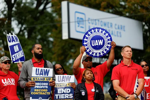Auto union workers, wearing red, hold signs supporting strikes.