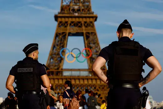 Two police officers stand in front of the Eiffel Tower, which is adorned with the Olympic rings.
