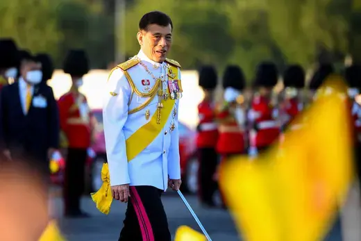 Thai King wears a white military dress uniform while carrying a sword and walking during a military procession.