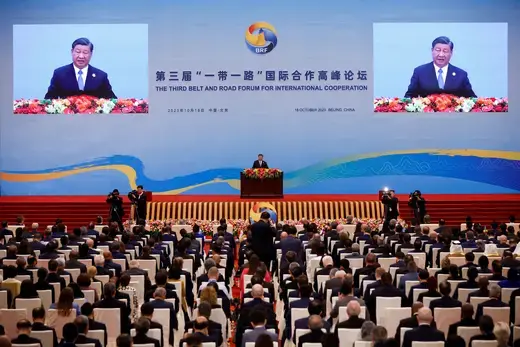 Chinese President speaks in front of an auditorium of seated people with a blue backdrop.