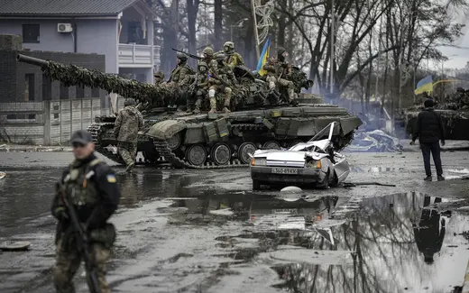 Ukrainian servicemen ride a tank next to a civilian vehicle destroyed during fighting between Russian and Ukrainian forces outside Kyiv, Ukraine, on April 2, 2022.