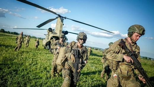 NATO soldiers run out of a helicopter carrying guns. 