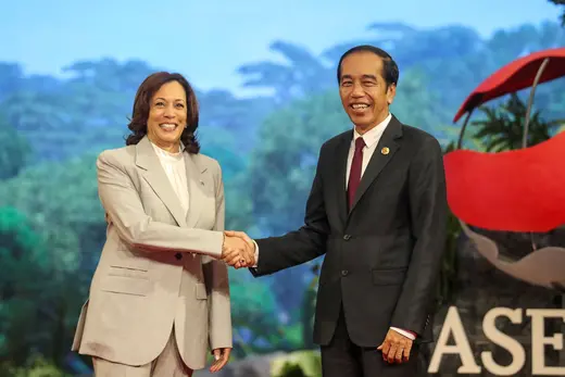 Vice President Kamala Harris wears a tan suit while shaking hands with Indonesian President Joko Widodo, who wears a black suit and maroon tie.