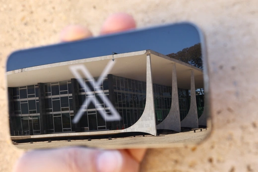 The logo of social media platform X is seen on a mobile phone next to a reflection of Brazil's Supreme Court in this illustration taken August 30, 2024, in Brasilia, Brazil.