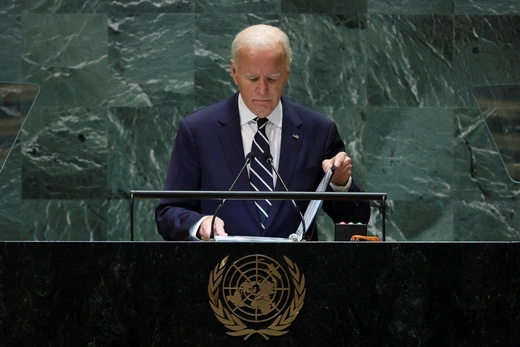 President Joe Biden stands in front of a UN podium looking down at his remarks in a binder.