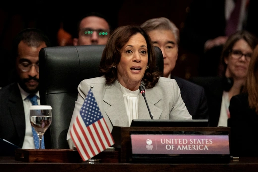 U.S. Vice President Kamala Harris wears a grey suit while sitting at a table with a small American flag.