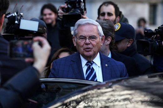 U.S. Senator Bob Menendez entering a car surrounded by photographers.