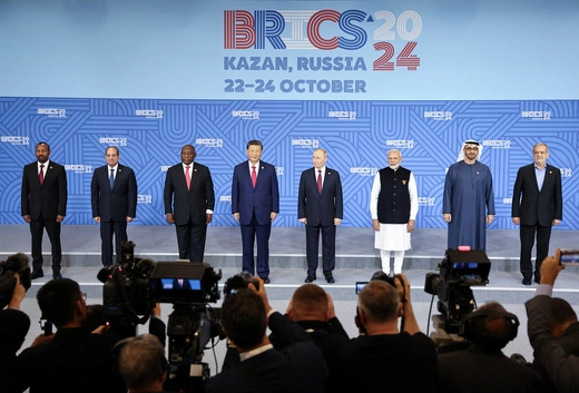 Eight leaders stand before a row of photographers with a backdrop displaying the name and logo for the BRICS summit in Kazan, Russia.