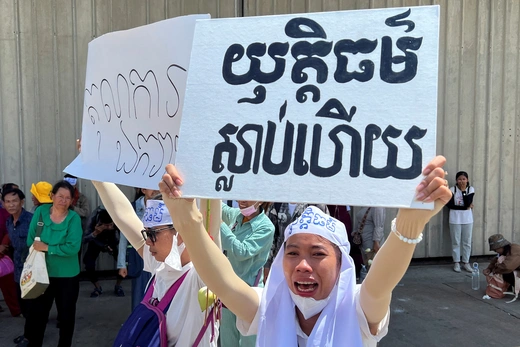 A woman stands holding up a white sign with black lettering.