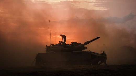 An Israeli Merkava battle tank is pictured surrounded by smoke while an IDF Israeli soldier stands atop the tank, as units regroup near the border of Gaza in Palestine.