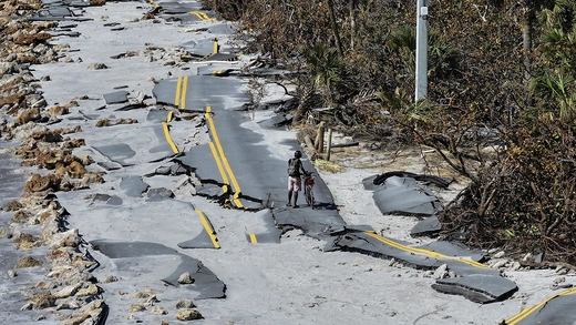 In an aerial view, a bicycle rider navigates a damaged road along the Gulf of Mexico on October 13, 2024 in Manasota Key, Florida. 