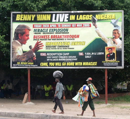 Street vendors walk past a billboard advertising visits by Pentecostal preachers to Nigeria on April 13, 2005 in Lagos, Nigeria.