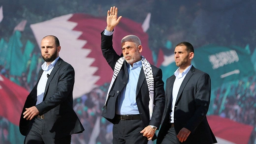 Hamas leader Yahya Sinwar stands with his arm raised, addressing a crowd as he walks toward a rally, accompanied by two other men.