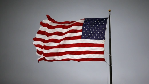 The flag of the United States billowing in the wind, backgrounded by an overcast grey sky.