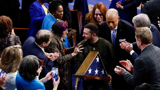 Volodymyr Zelenskyy holds a folded up U.S. flag in a case while he walks through a crowd of people congratulating him, clapping, and taking his photo after he gave remarks at the U.S. Capitol.