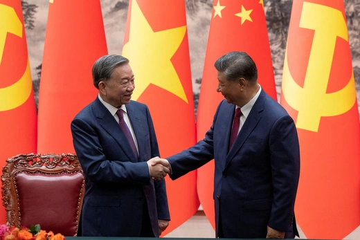 Vietnam and China's leaders wear blue suits while shaking hands in front of red and yellow flags. 