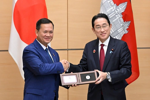 Cambodian Prime Minister Hun Manet wears a blue suit while shaking hands with then-Japanese Prime Minister Kishida Fumio, who wears a black suit.