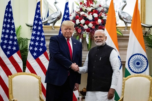 President Trump wears a blue suit while shaking the hand of Prime Minister Narendra Modi, who wears a black tunic and white shirt.