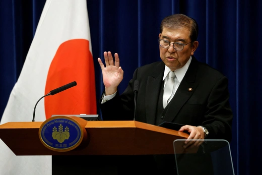 Japanese Prime Minister Ishiba Shigeru stands behind a podium in front of the Japanese flag while speaking at a press conference in Tokyo.