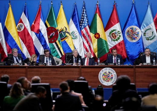 Delegates at a session of Fifty-Second General Assembly of the Organization of American States sit at a table in front of flags representing the U.S. and Latin American countries.