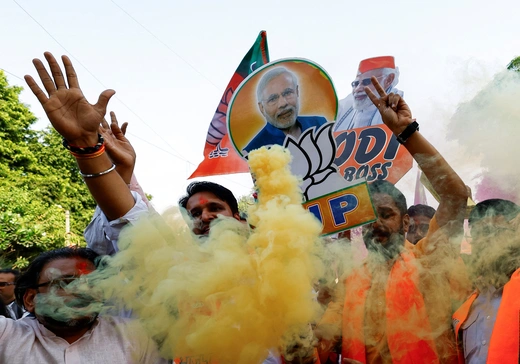 Supporters of India's ruling party celebrate during an election rally, waving flags, holding posters featuring Prime Minister Narendra Modi, and surrounded by clouds of colorful smoke.