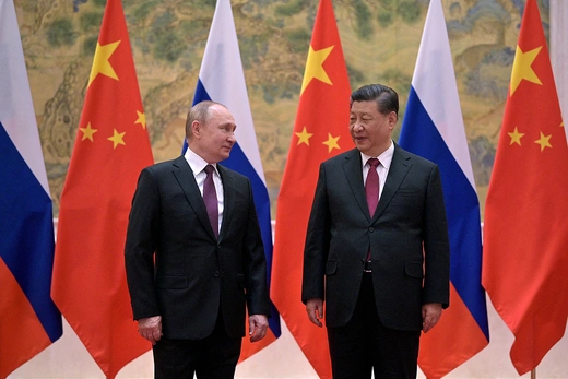 Russian President Vladimir Putin stands next to Chinese President Xi Jinping in front of a display of Russian and Chinese flags.