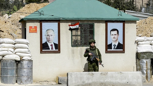 A member of the Russian military police guards a checkpoint on the outskirs of Damascus adorned with portraits of Russian President Vladimir Putin (L) and former Syrian President Bashar al-Assad (R) in March 2018.