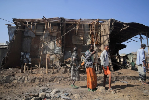 People stand in front of the rubble of a bombed building.