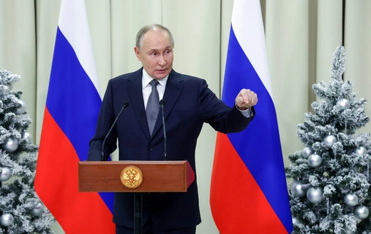 Russian President Vladimir Putin standing at a lectern, flanked by Russian flags