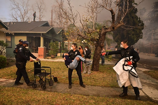 Police officers remove an elderly resident from her home during the Eaton Fire in Altadena, California, on January 8, 2025.