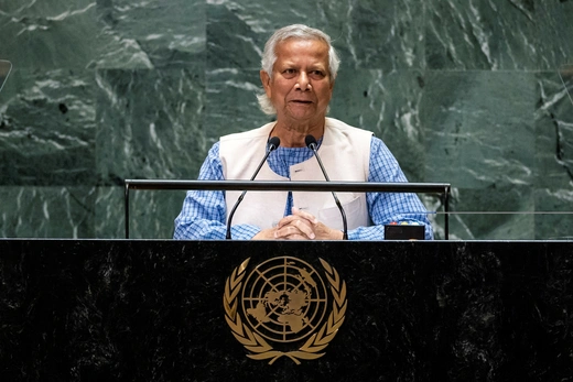 Muhammad Yunnus stands at a podium at the UN General Assembly wearing a white vest and blue shirt.