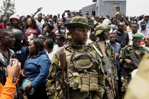 Armed soldiers stand in front of a packed crowd of civilians in front of a building in DRC.