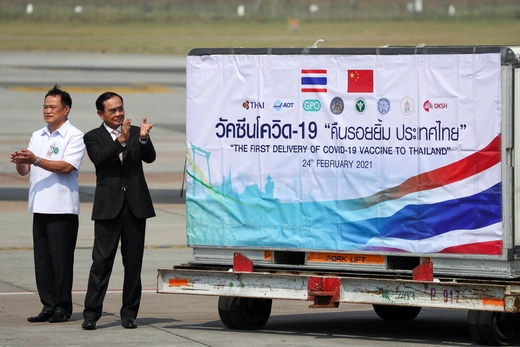 Officials stand on an airport tarmac next to a trailer applauding.