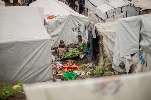 A woman sits on the ground surrounded by white humanitarian relief tents. 