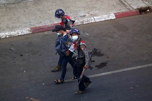 Two helmeted police officers escort a journalist as they arrest him, walking down the street.