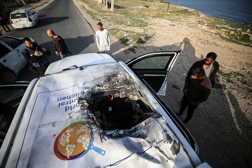 Palestinians stand next to a vehicle with a World Central Kitchen logo on top of it and a hole in the car roof in this image from above.